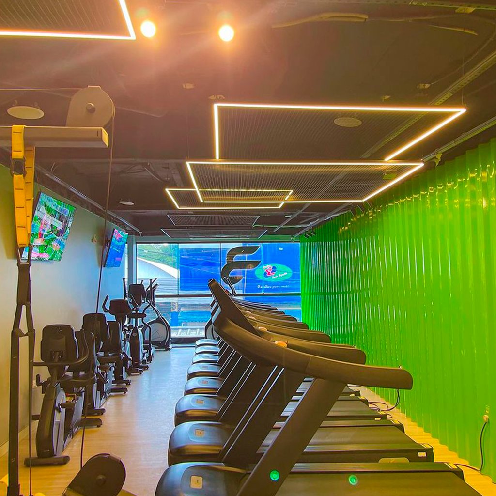 Área de cardio com esteiras e parede verde iluminada